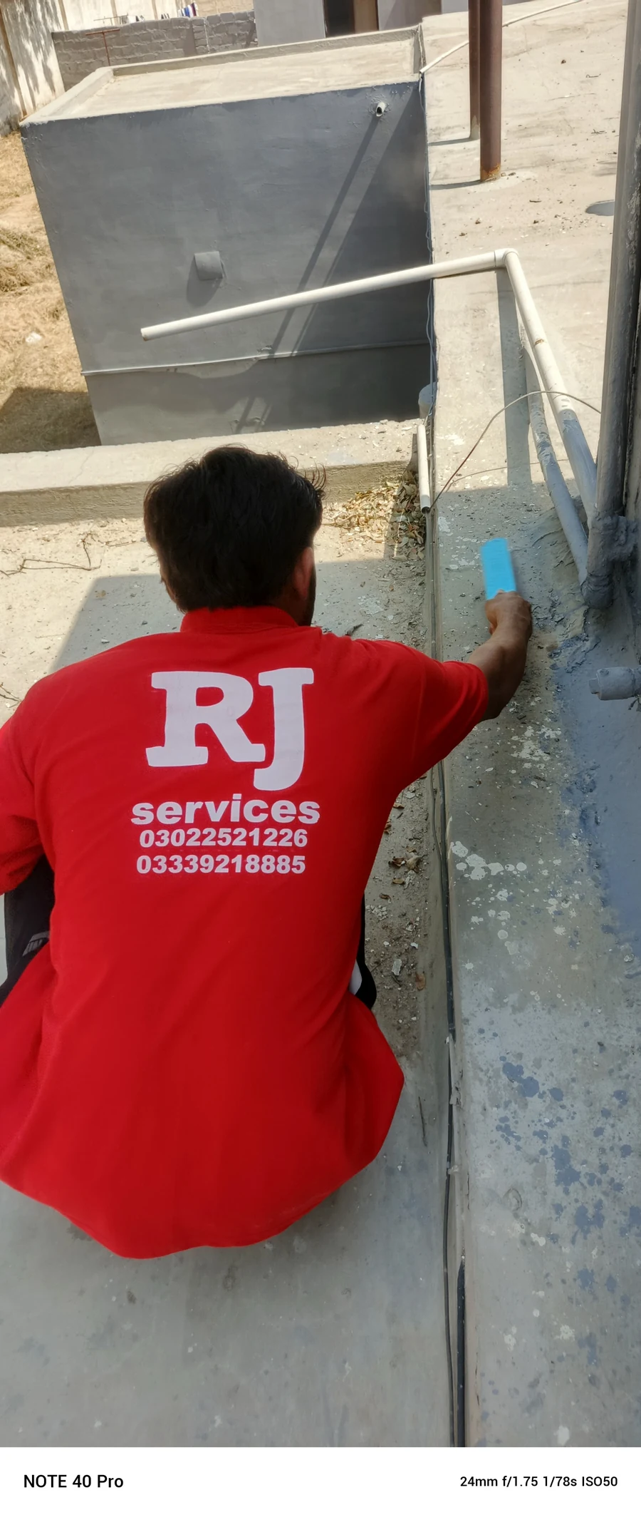Rana Jees Fumigation Services technician preparing an exterior surface beside a roof edge